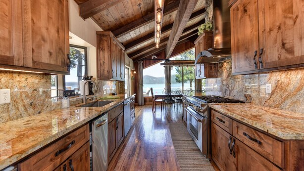 A kitchen with wooden cabinets, granite countertops, and a view of a lake.