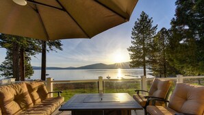 A patio with a table and two sofas, overlooking a lake with a sunset.