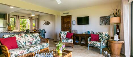 A spacious living room with wicker furniture, a ceiling fan, and a television on the wall.