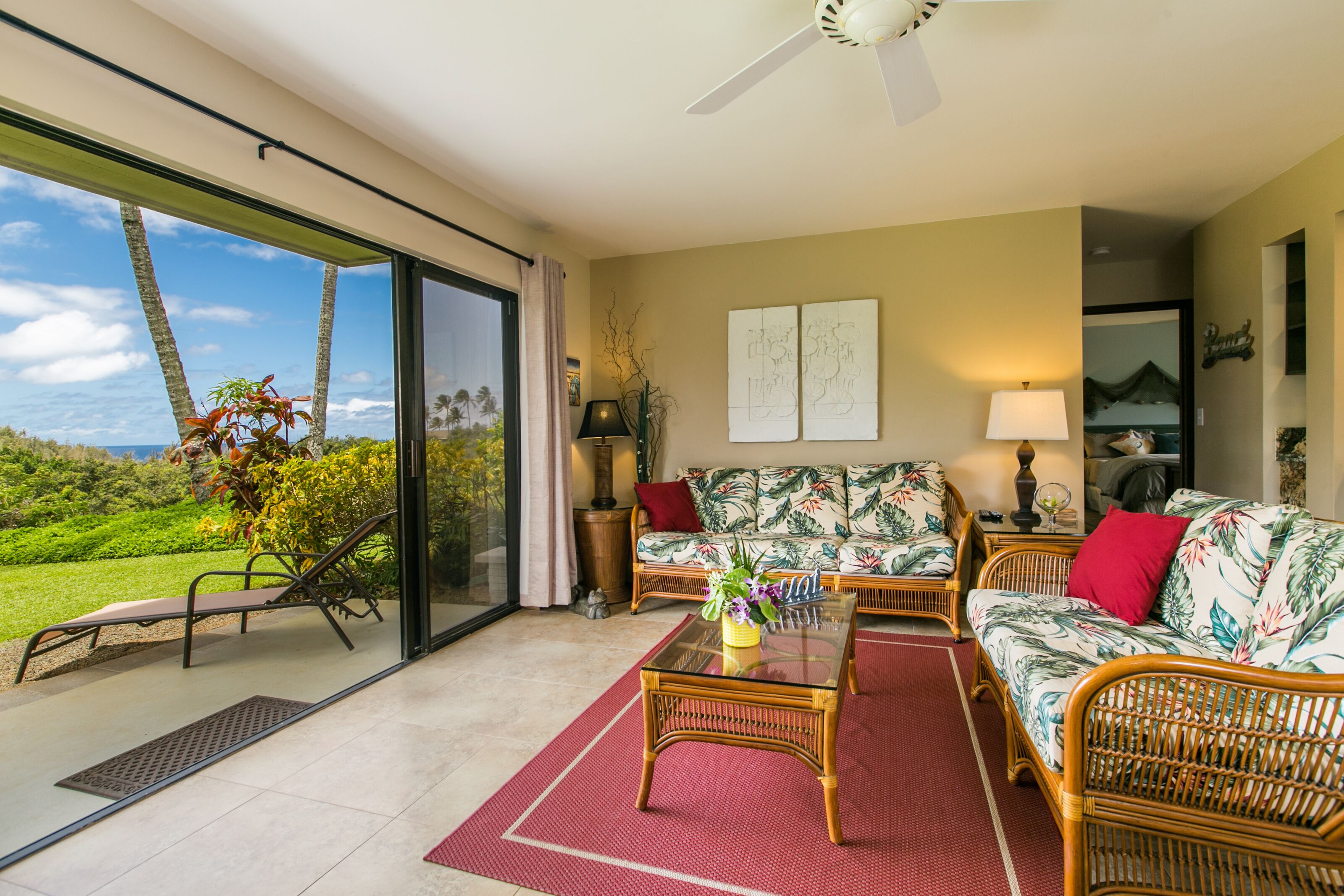 Un amplio salón con un gran ventanal corredera que da a un balcón, muebles de mimbre y vistas al exterior.
