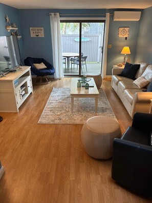 A living room with a sofa, ottoman, coffee table, and a view of the backyard.