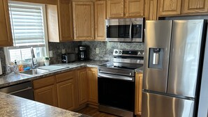 A modern kitchen with wooden cabinets, stainless steel appliances, a granite countertop, and a window with blinds.
