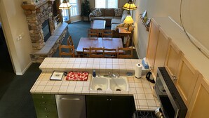 A kitchen with a tiled countertop, a sink, and a dishwasher. There is a dining area with a table and chairs, and a living room with a sofa and a lamp. - Lovely, 3 Bdr, 2 Ba Walk To Eagle Chair, On Sierra Star Golf Course! (Mammoth Lakes)