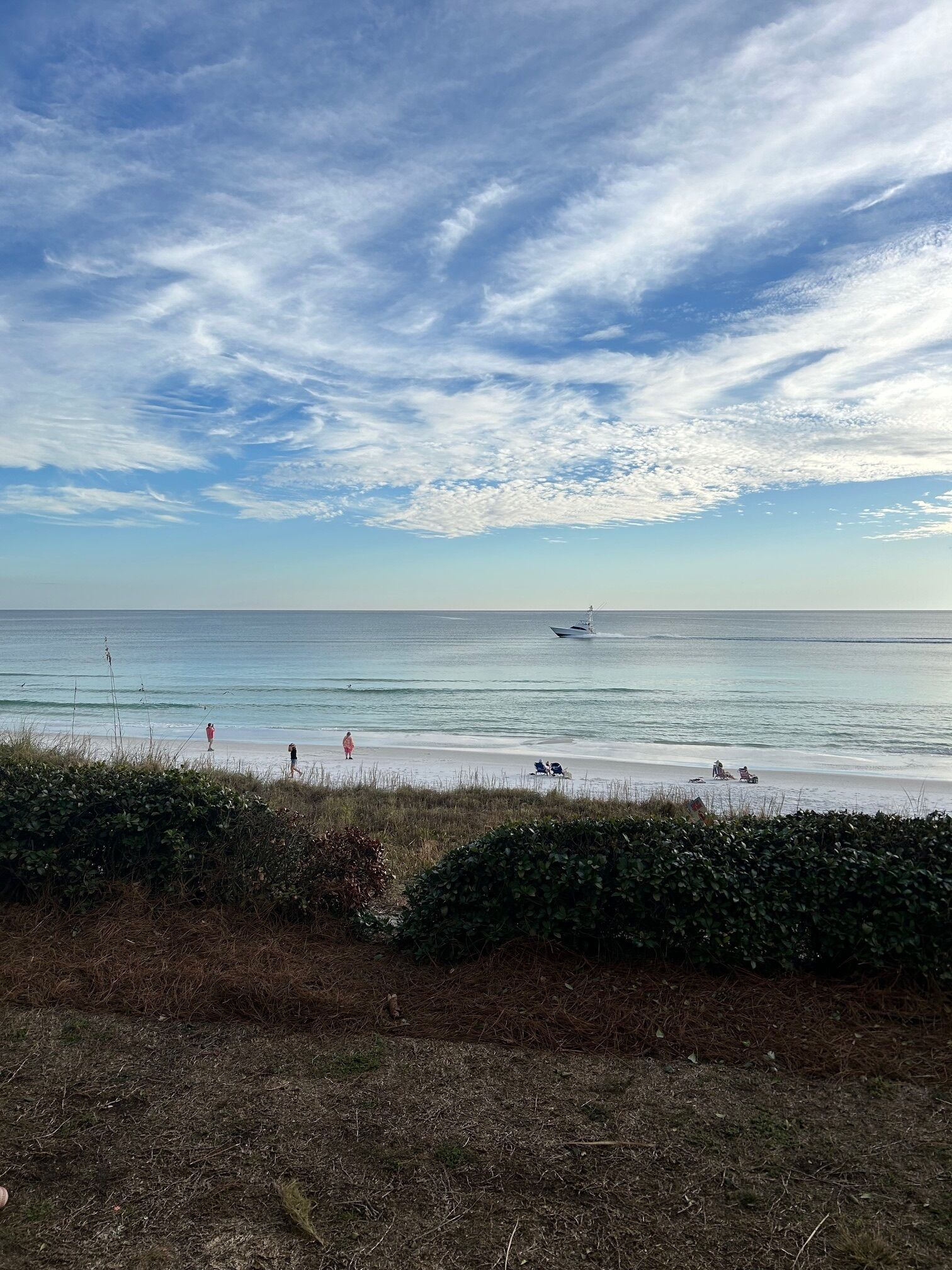 A beach with a clear sky, calm sea, and distant boats.