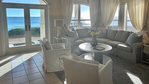 Un salon spacieux doté d’une grande fenêtre offrant une vue sur l’océan, d’un canapé blanc, d’une table basse ronde et d’un ventilateur de plafond.