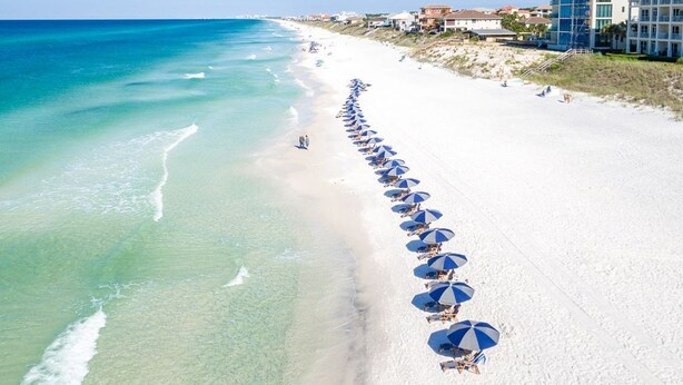 Une plage bordée d’une rangée de parasols et un immeuble à plusieurs étages.