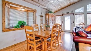 A dining area with a wooden table and chairs, a red leather couch, and a wooden ceiling. - Serenity Pines (Yosemite National Park)