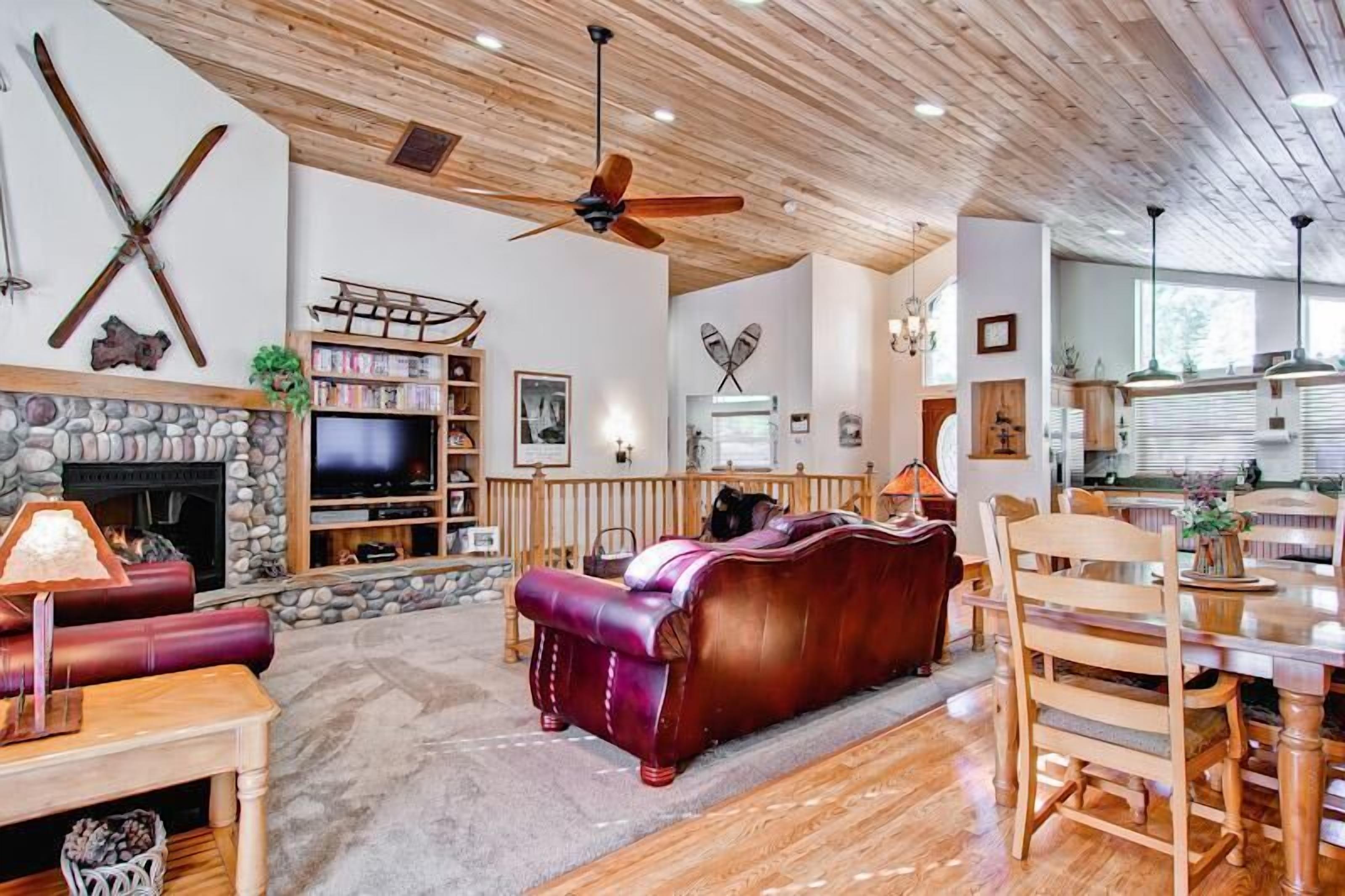 A spacious living room with a stone fireplace, leather sofa, wooden dining table, and ceiling fans.
