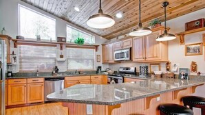 A kitchen with wooden cabinets, a granite countertop, and a large island with bar stools. - Serenity Pines (Yosemite National Park)