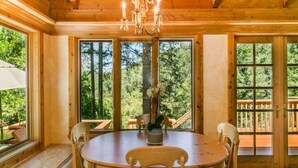 Un comedor de madera con candelabro, ventanas amplias y vista al bosque.