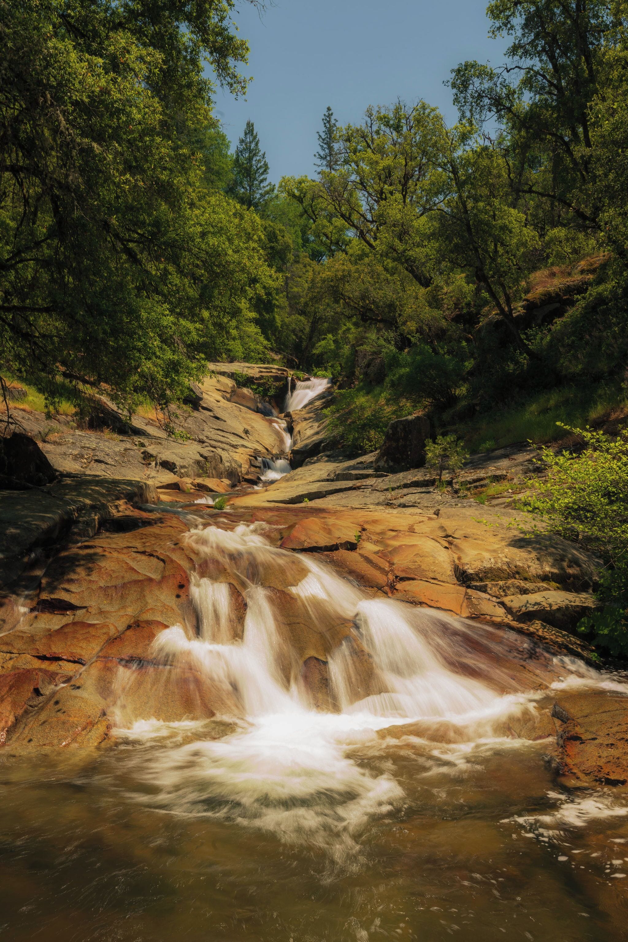Un paisaje natural con una cascada que fluye sobre rocas, rodeado de frondosa vegetación verde.