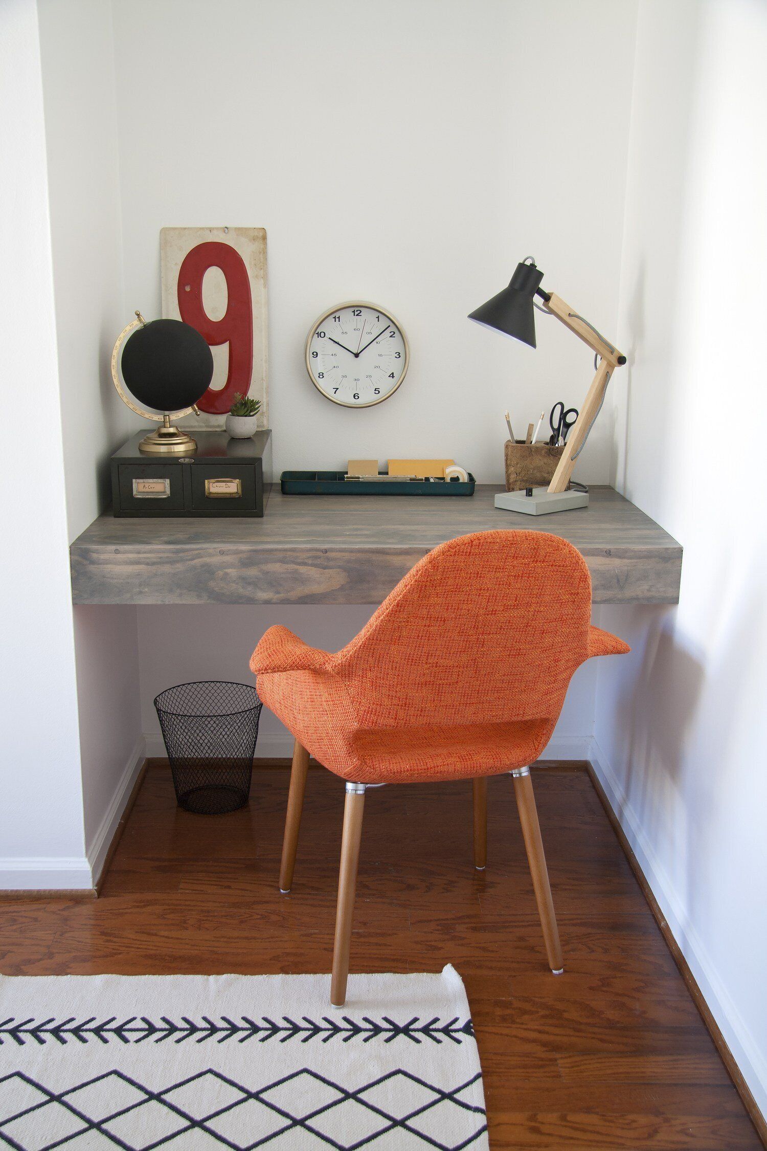 A study area with a desk, a chair, a clock, a lamp, and a waste basket.
