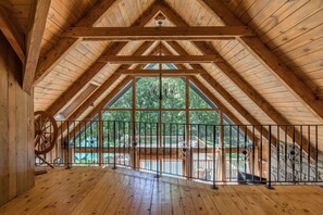 A spacious attic room with wooden beams, large windows, and a balcony with a metal railing.