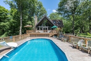A swimming pool with a wooden deck, lounge chairs, and a wooden deck with a railing.