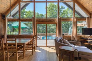 A spacious room with a large wooden ceiling, a pool visible through the glass doors, and a cozy seating area with a sofa and a table.