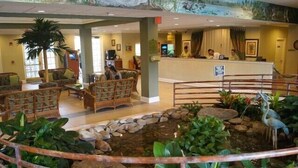 A lobby with wicker furniture, a reception desk, and a decorative pond with a heron statue. - Bahama Bay Resort Unit 28703 - 3BR 2BA Ground Floor Condo - Great Value (Davenport)