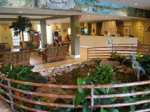 Un hall con mobiliario de mimbre, una recepción y un estanque decorativo con una estatua de garza.
