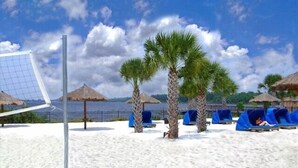 A beach with a volleyball net, palm trees, and blue lounge chairs. - Bahama Bay Resort Unit 28703 - 3BR 2BA Ground Floor Condo - Great Value (Davenport)