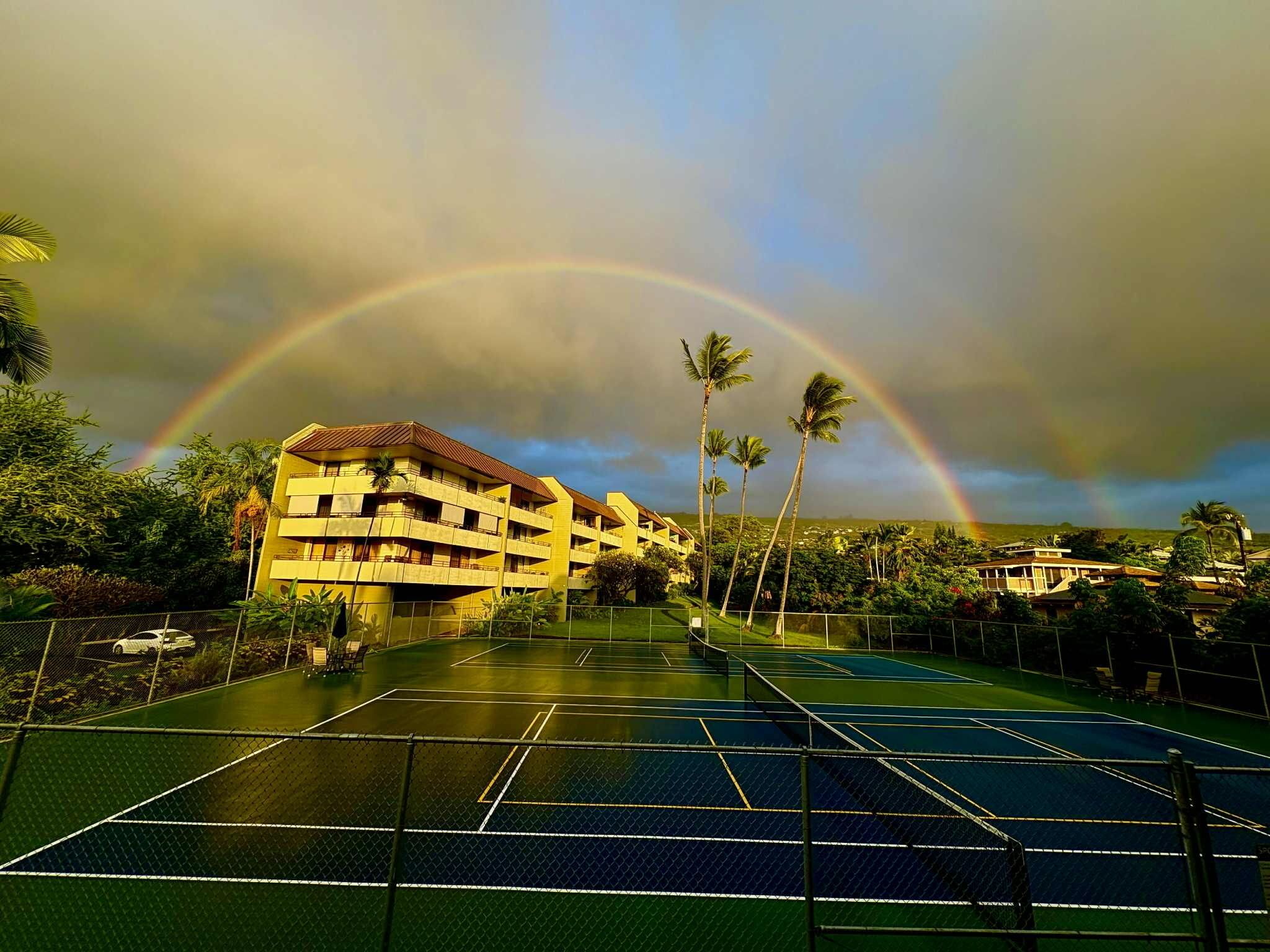 En tennisbana med en byggnad i bakgrunden och en regnbåge.
