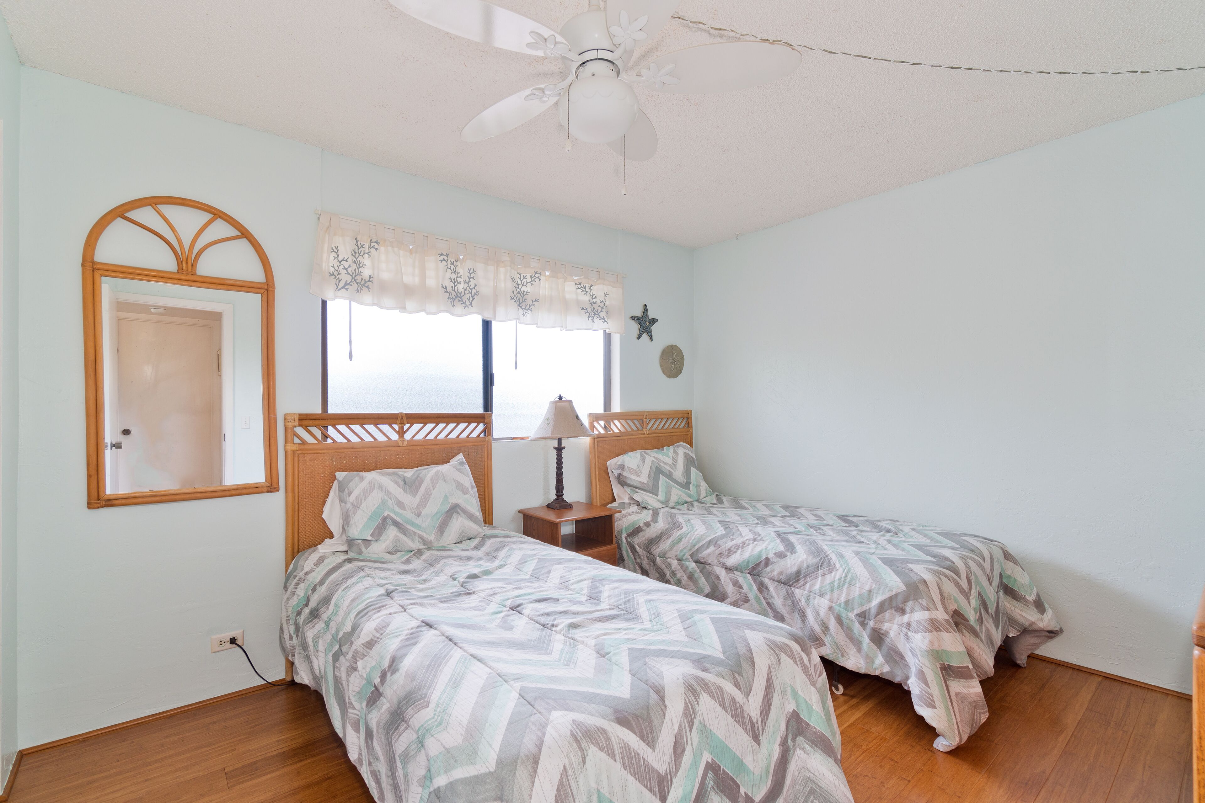 Ein Schlafzimmer mit zwei Betten, einem Deckenventilator, einem Fenster mit Vorhängen, einem Spiegel und einer Sternen-Dekoration an der Wand.