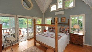 Une chambre à coucher avec un grand lit, une tête de lit en bois, une table de chevet et une fenêtre donnant sur un lac.