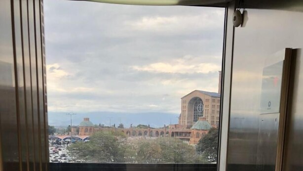 An elevator with a view of a building with a large arched window and a parking lot with cars. - Hotel Cathedral (Aparecida)