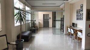 A spacious, well-lit hallway with a seating area, a desk, and a staircase leading to an elevator. - Hotel Cathedral (Aparecida)