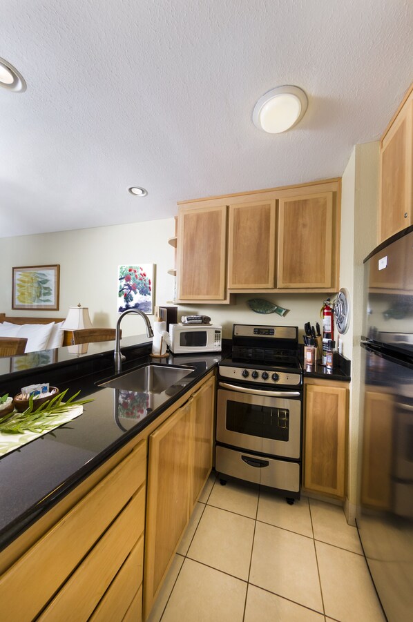 A modern kitchen with wooden cabinets, a stainless steel sink, a microwave, an oven, and a refrigerator.