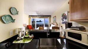 Una cocina moderna con un lavamanos de acero inoxidable, una cafetera y un microondas. Hay peces decorativos en la pared y se ve un balcón.