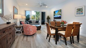 A modern living room with a dining area, large windows, and a ceiling fan.