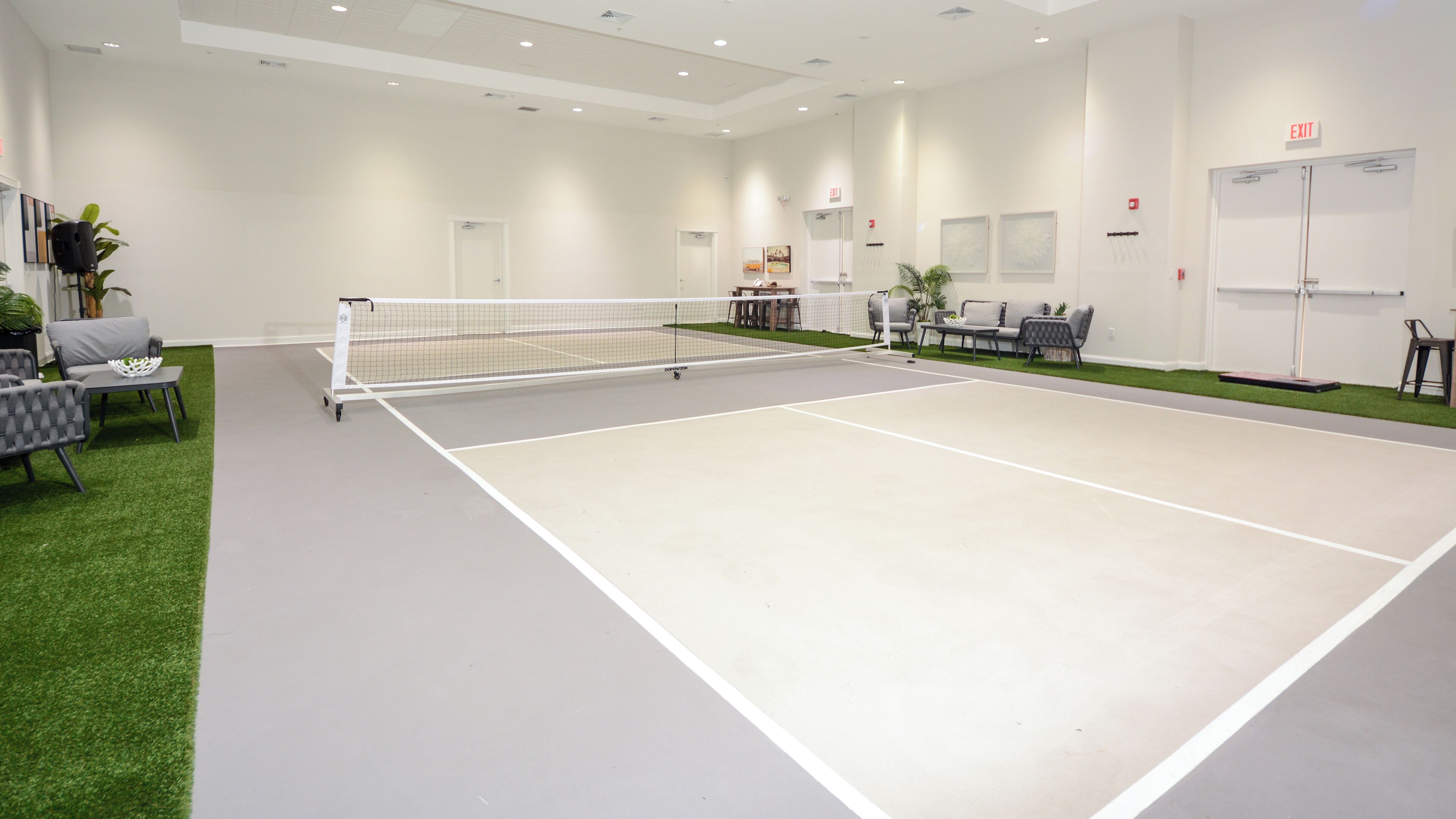 Una cancha de tenis con red, zona de estar y señalización de salida.