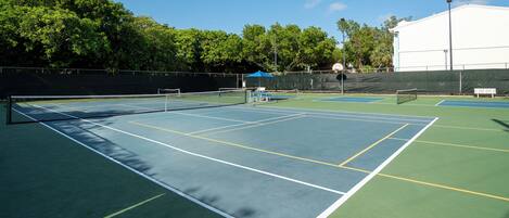 An outdoor tennis court with multiple courts, a net, and a covered seating area.