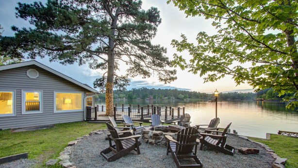Una cabaña junto al lago con un balcón, mobiliario exterior y vistas al lago.