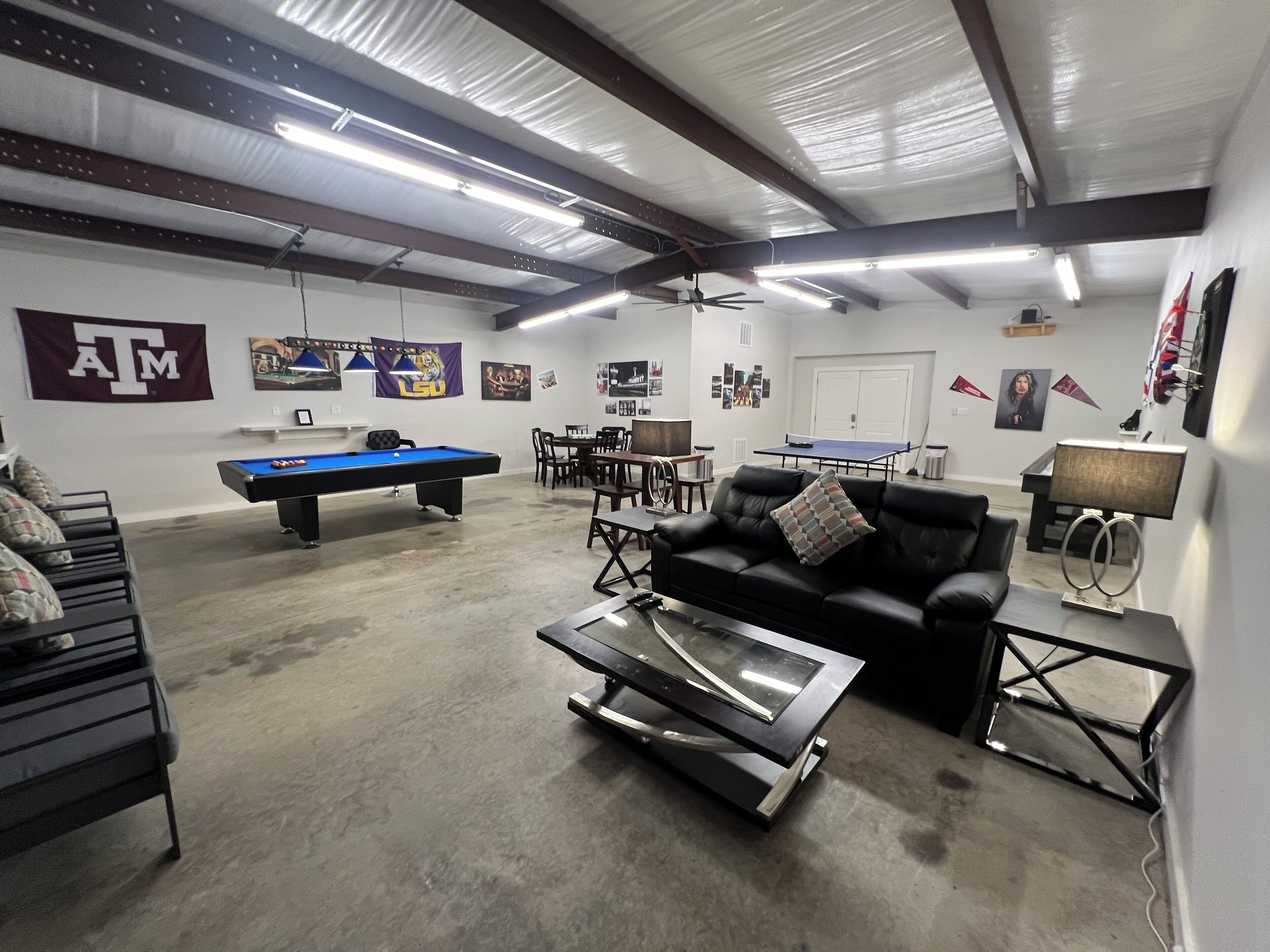 Une pièce spacieuse équipée d’une table de billard, d’un canapé en cuir noir, d’une table de ping-pong et d’un ventilateur de plafond.