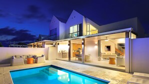 Una casa moderna con piscina, mobiliario exterior y un interior bien iluminado.