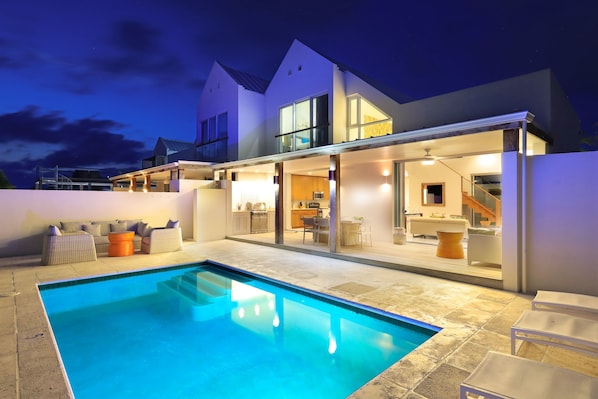 Une maison moderne dotée d’une piscine, d’un espace extérieur aménagé et d’un intérieur bien éclairé.