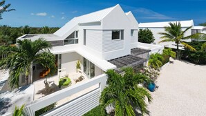Una casa moderna de color blanco con techo plano, ventanas amplias y un patio con mobiliario exterior.