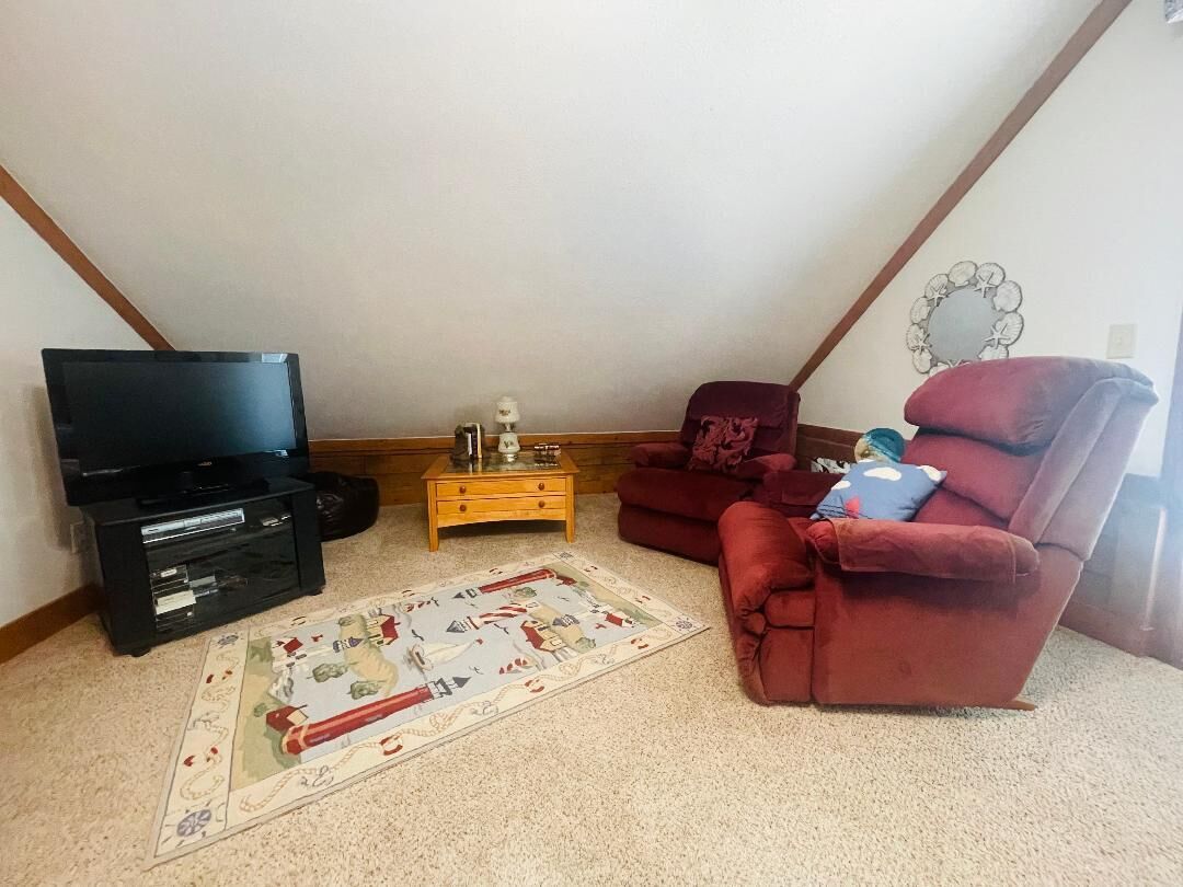 A cozy attic room with a black entertainment unit, a red recliner, and a patterned rug.