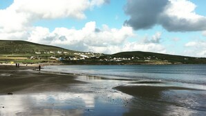A coastal landscape with a sandy beach, calm water, and a distant village with houses. - Self-Catering Holiday Home in Beautiful Ventry (Dingle)
