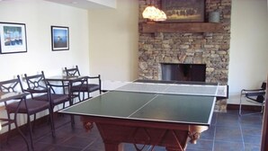 Une table de ping-pong dans une pièce aux murs de pierre, avec une cheminée et des tableaux encadrés accrochés au mur.