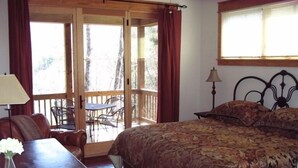 Une chambre avec un grand lit, un bureau avec une lampe et une vue sur une terrasse aménagée avec du mobilier d’extérieur.