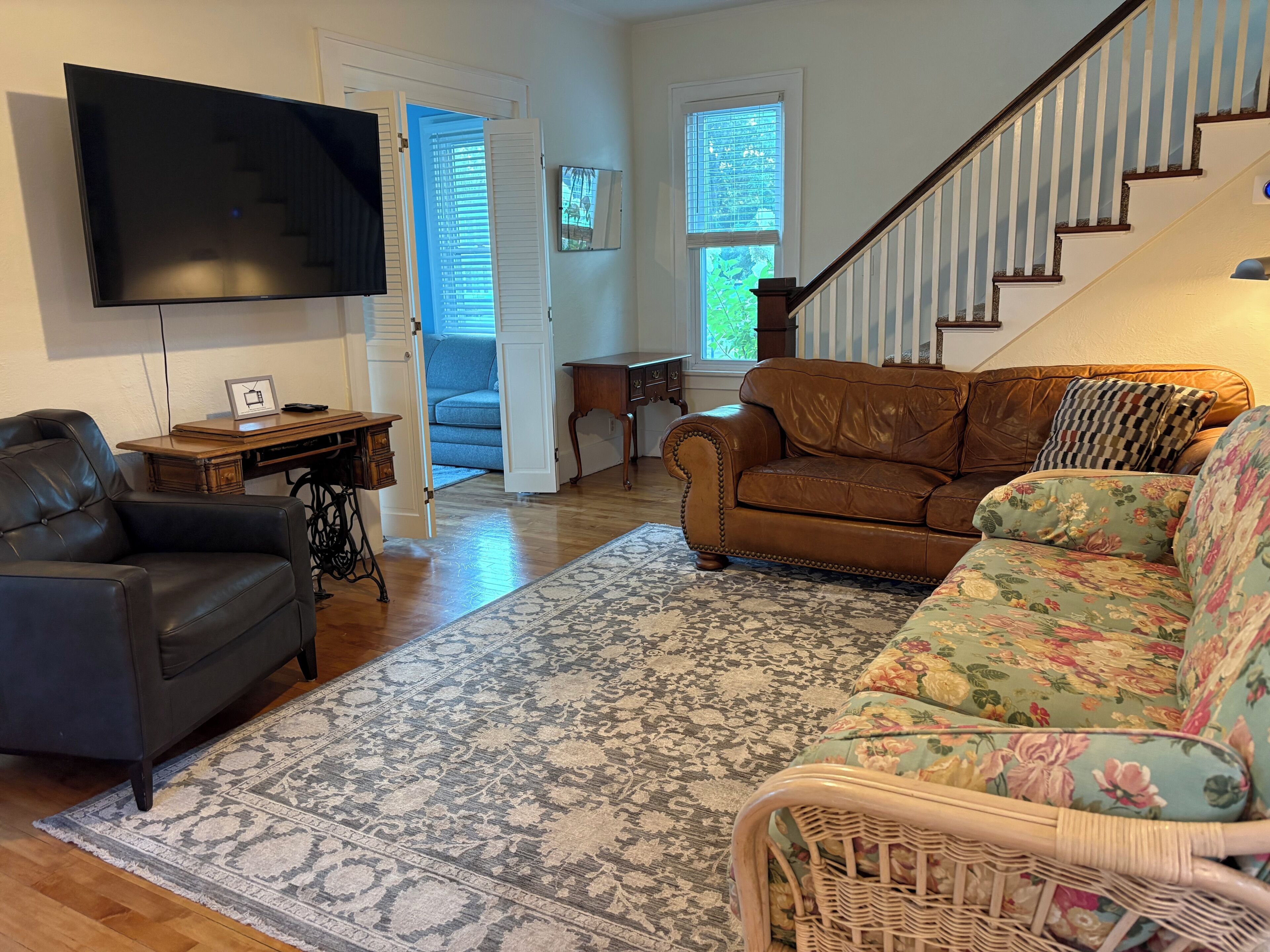A living room with a leather sofa, a floral armchair, a television, and a staircase.