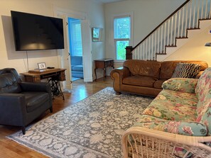 A living room with a leather sofa, a floral armchair, a television, and a staircase.