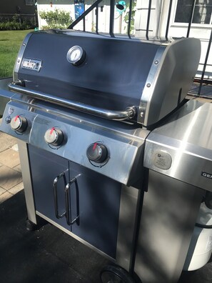 A portable gas grill with two burners and a side burner, featuring a digital thermometer and a red ignition knob.