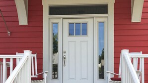 Une maison rouge avec une porte d’entrée blanche, deux rampes de garde-corps blanches et un escalier en bois menant à la porte.