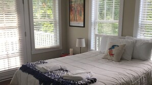 Une chambre à coucher avec un lit, un ventilateur de plafond et des fenêtres équipées de stores.