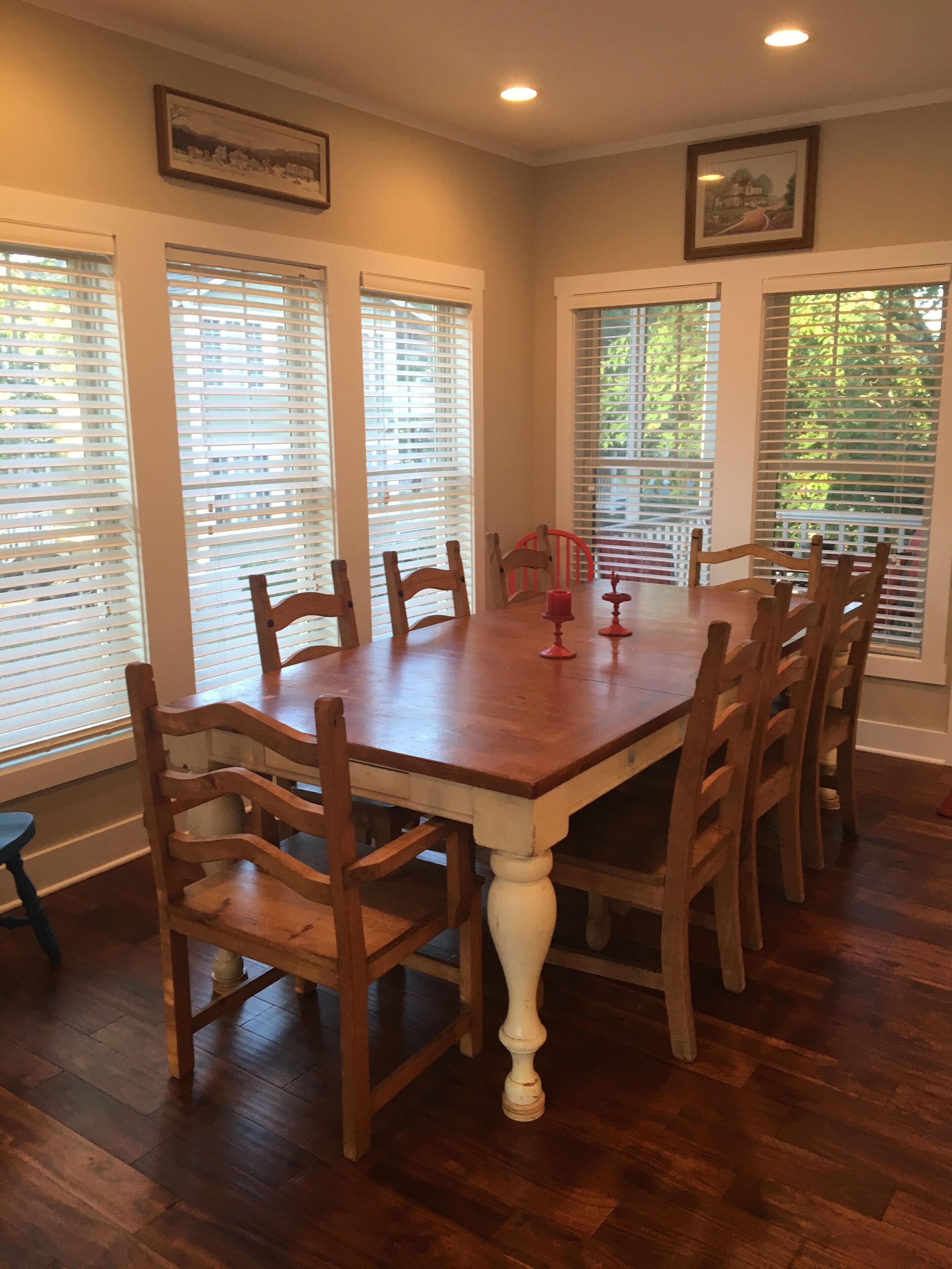Comedor con mesa y sillas de madera, ventanas grandes con persianas y una araña.