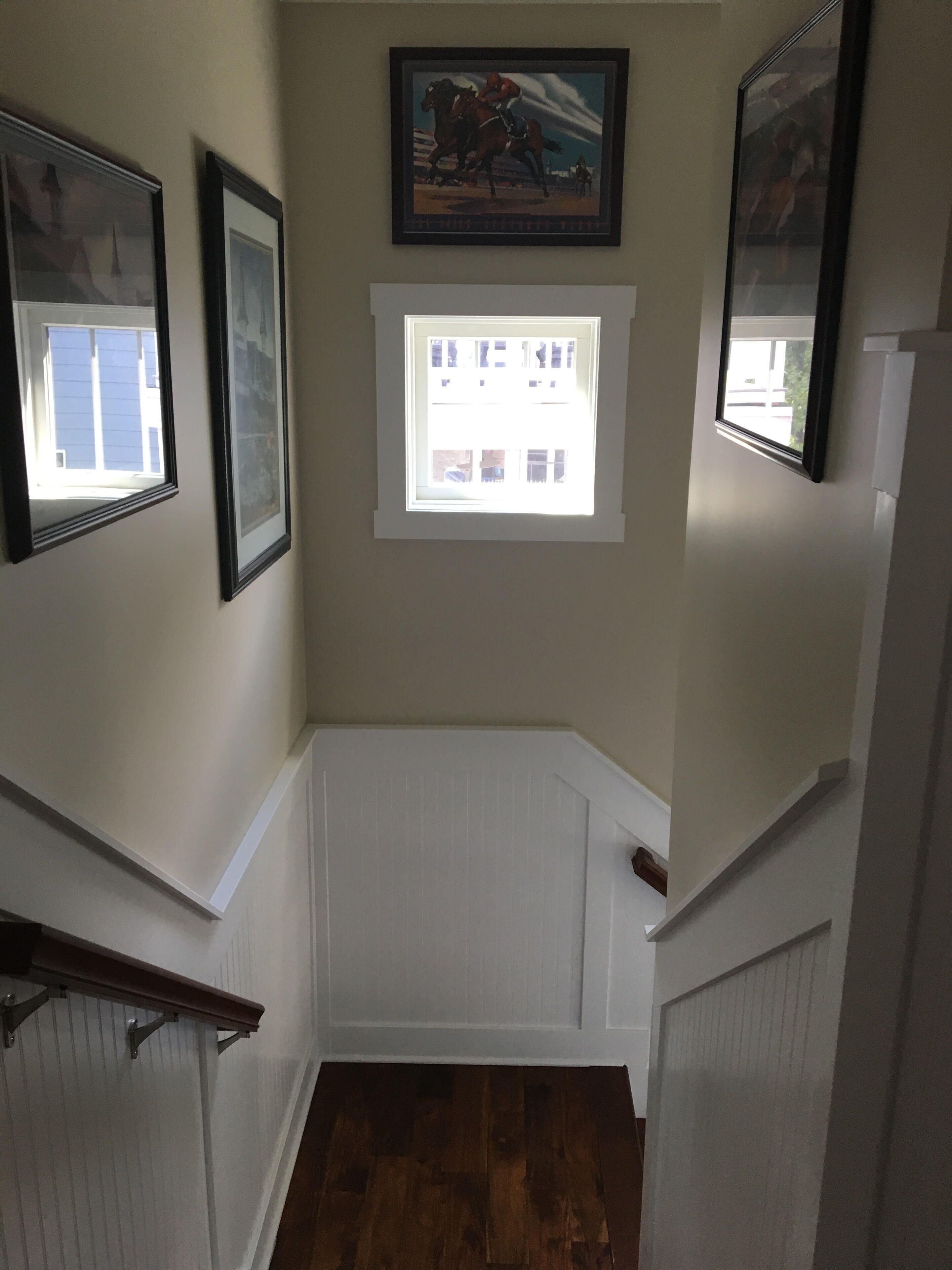 A hallway with a wooden floor, white wainscoting, and framed pictures on the walls.