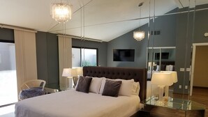Une chambre d’hôtel moderne dotée d’un grand lit, d’une paroi en verre, d’un téléviseur à écran plat et d’un lustre.