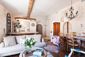 A cozy living room with a sofa, coffee table, and a dining area with chairs and a chandelier.